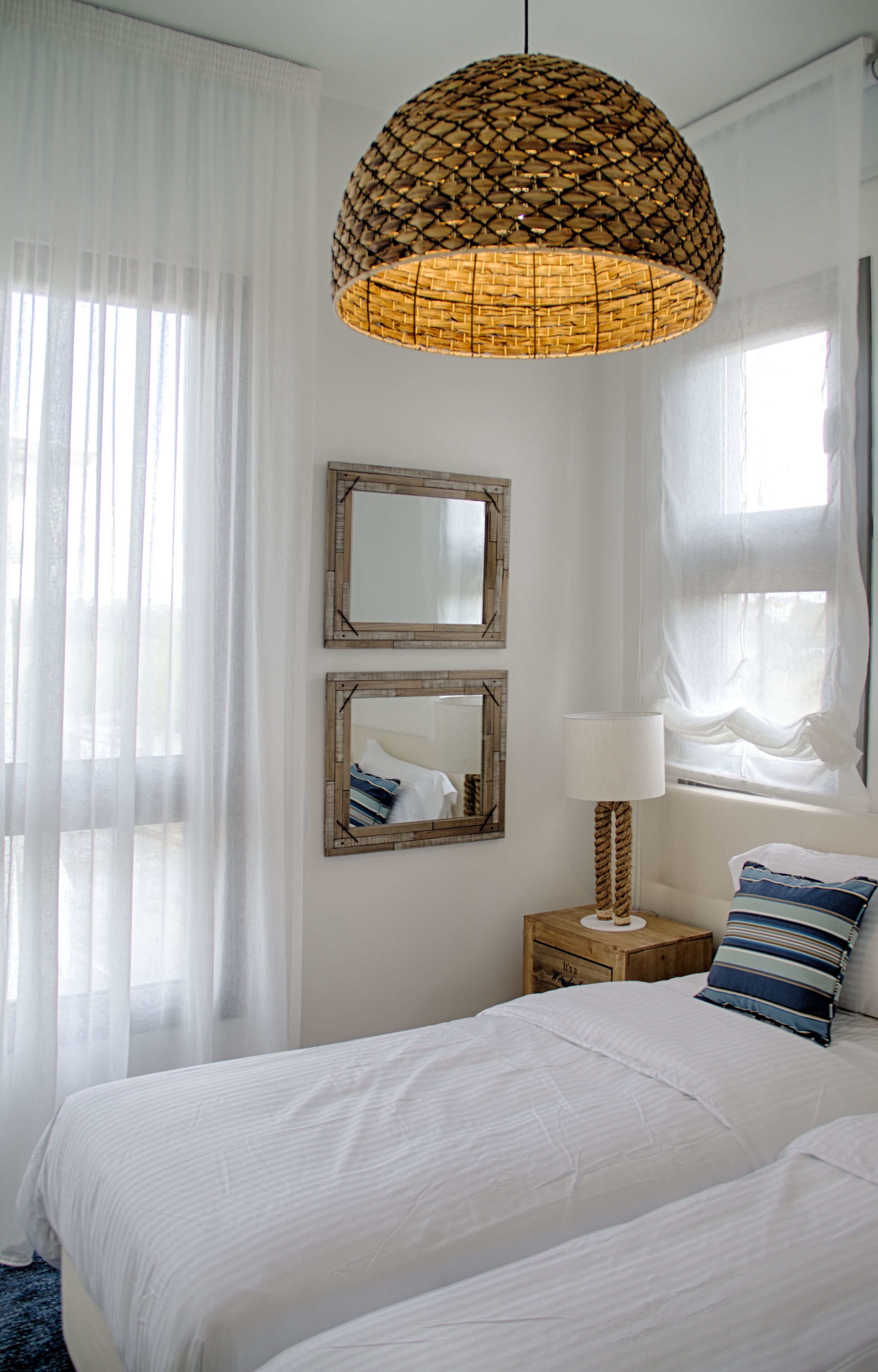 A bedroom with a large bed, two wall mirrors, a bedside lamp, and sheer curtains.