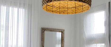 A bedroom with a large bed, two wall mirrors, a bedside lamp, and sheer curtains.