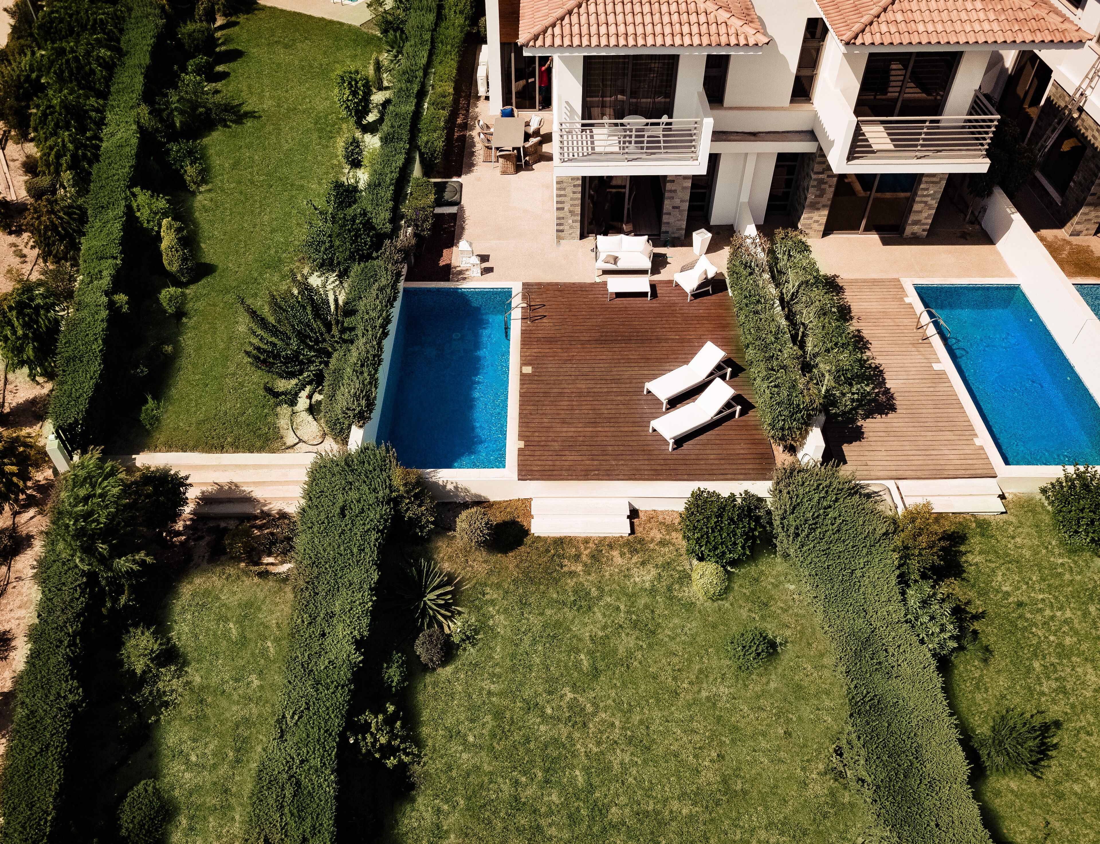 Una casa moderna con dos piscinas, una terraza de madera y un césped cuidado.