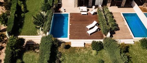 Una casa moderna con dos piscinas, una terraza de madera y un césped cuidado.