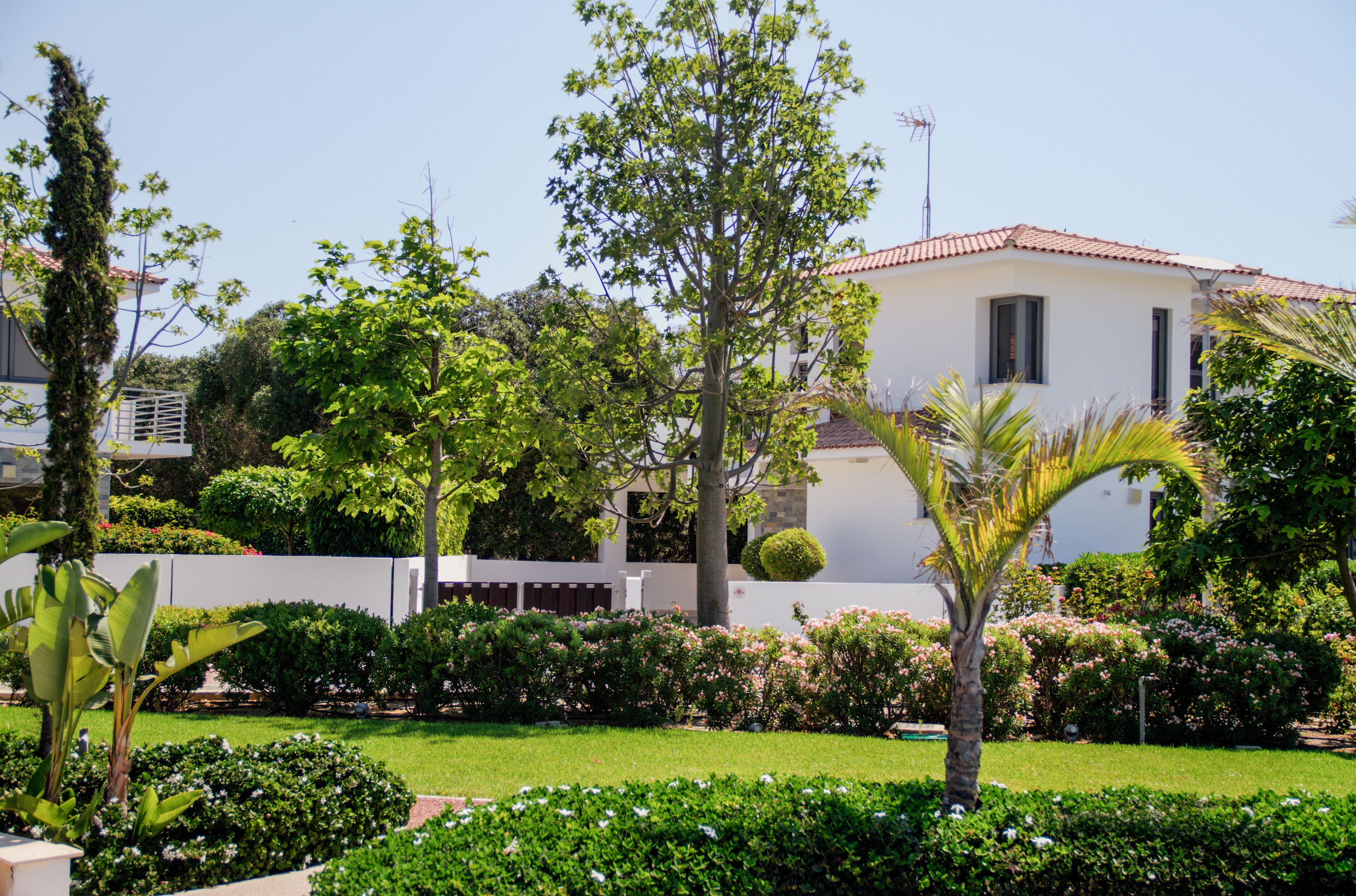 A white building with a red-tiled roof, surrounded by lush greenery and well-maintained gardens.
