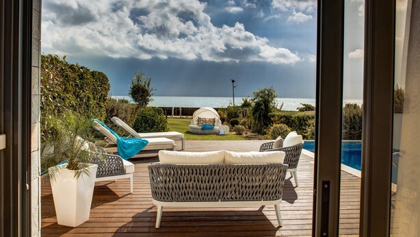 A deck with outdoor furniture, a pool, and a view of the sea. - Atlantis Gardens (Mazotos)