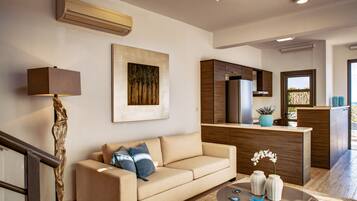 A modern living room with a beige sofa, a glass coffee table, and a kitchen area with wooden cabinets and a refrigerator.