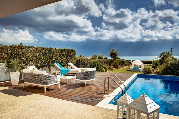 A poolside area with lounge chairs, a pergola, and a view of the ocean.