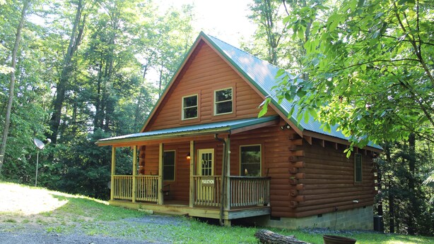 A log cabin with a porch, surrounded by trees.