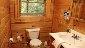 A wooden cabin bathroom with a toilet, sink, and a window above the toilet.