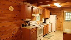 A wooden cabin kitchen with wooden cabinets, a stove, a refrigerator, and a clock on the wall.