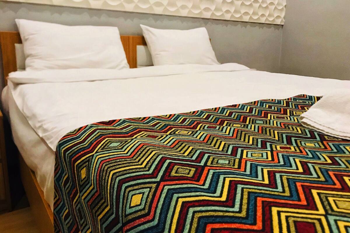 A bed with white bedding and a colorful geometric-patterned throw blanket.