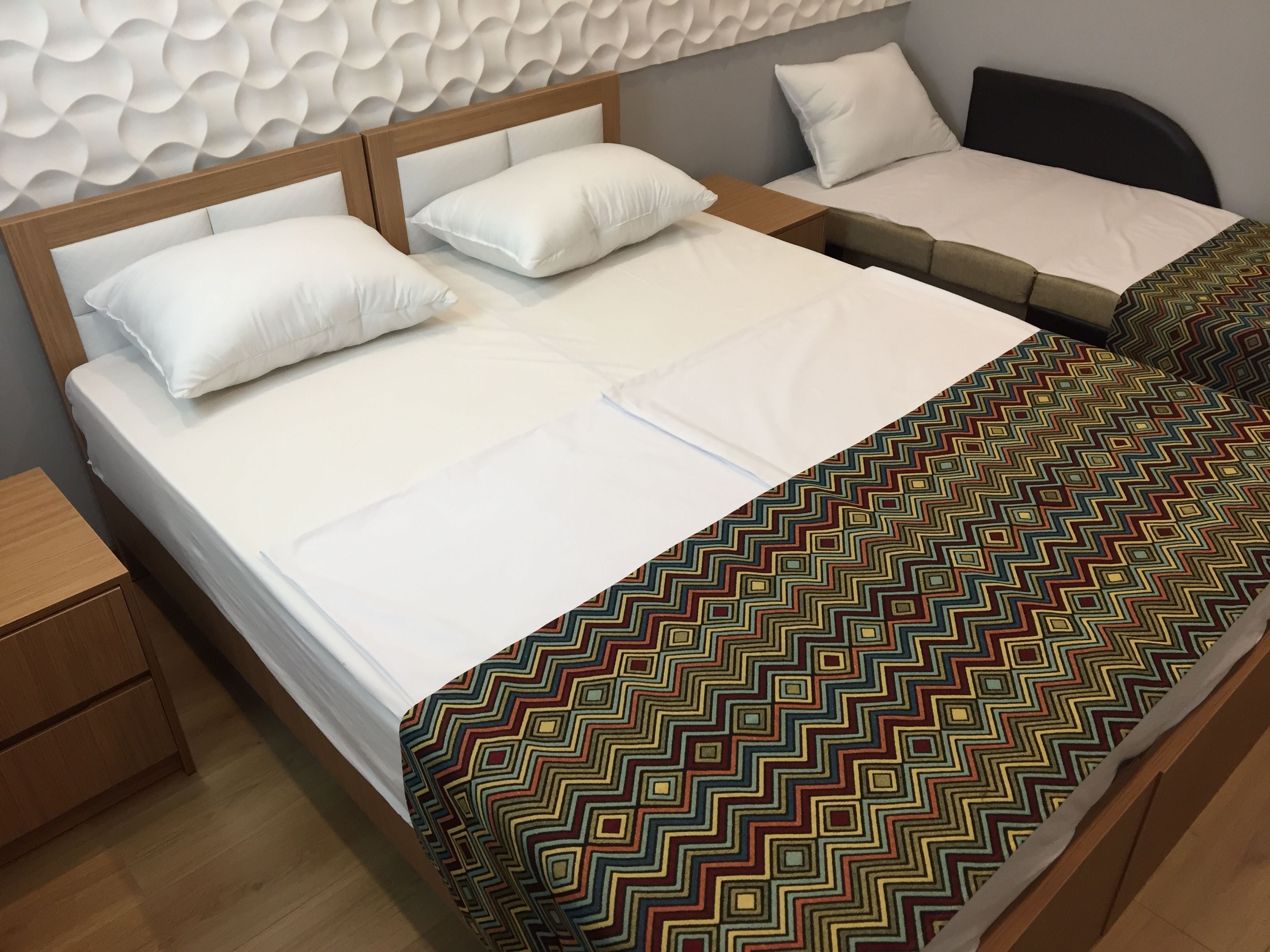 A double bed with white linens and a colorful zigzag-patterned blanket.