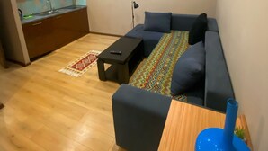 A modern living space with a kitchen, a sofa set, a TV, and a blue vase on a wooden table. - Downtown Hotel Tbilisi (Tbilisi)
