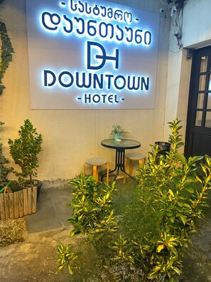 A sign for the Downtown Hotel with a neon sign and a small outdoor seating area with two stools and a table. - Downtown Hotel Tbilisi (Tbilisi)