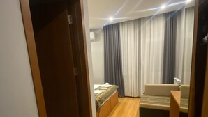 A modern bedroom with a wooden floor, a bed with a patterned bedspread, a sofa, a small table, and a wardrobe. - Downtown Hotel Tbilisi (Tbilisi)