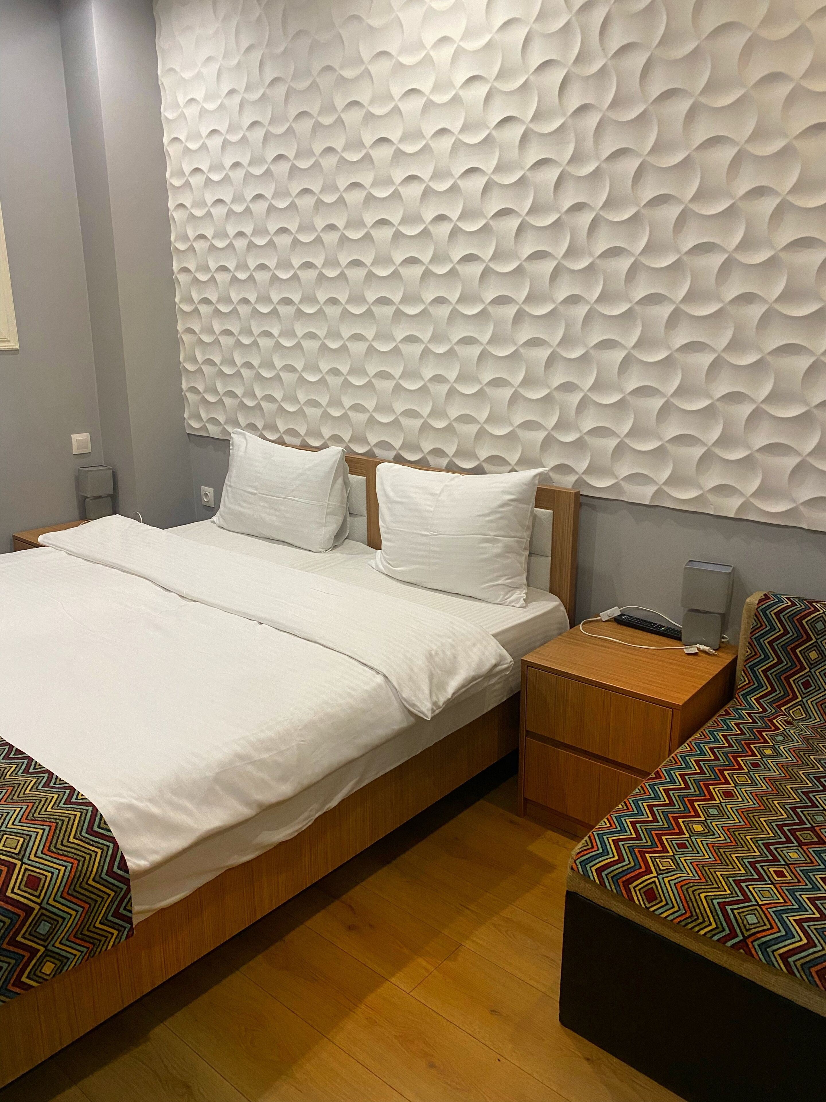 Ein modernes Schlafzimmer mit einem großen Bett, einem Holz-Nachttisch, einer gemusterten Couch und einer strukturierten Wand.