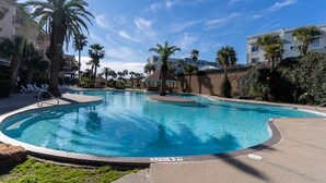 A swimming pool with lounge chairs and palm trees, surrounded by buildings. - Seaglass Serenity M112 NEW IN '24 (Galveston)