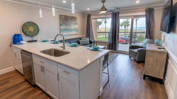 A spacious kitchen with a large island, a dining area with a view, and a living room with a TV. - Seaglass Serenity M112 NEW IN '24 (Galveston)