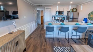 A modern kitchen with a central island, bar stools, and a dining table. - Seaglass Serenity M112 NEW IN '24 (Galveston)