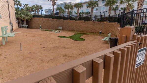 A sandy play area with green grass patches, benches, and a pet waste sign.