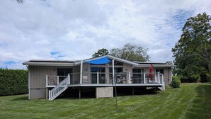 A modern two-story house with a covered patio, a staircase, and a well-maintained lawn. - Cleves Point Estates Home, Private sandy beach (Greenport)
