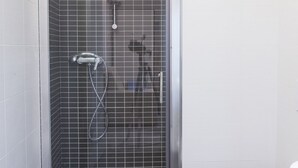 A shower with a glass door, a handheld showerhead, and a wall-mounted faucet.