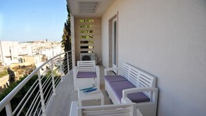 A balcony with white furniture, including two chairs and a small table, and a view of the cityscape.