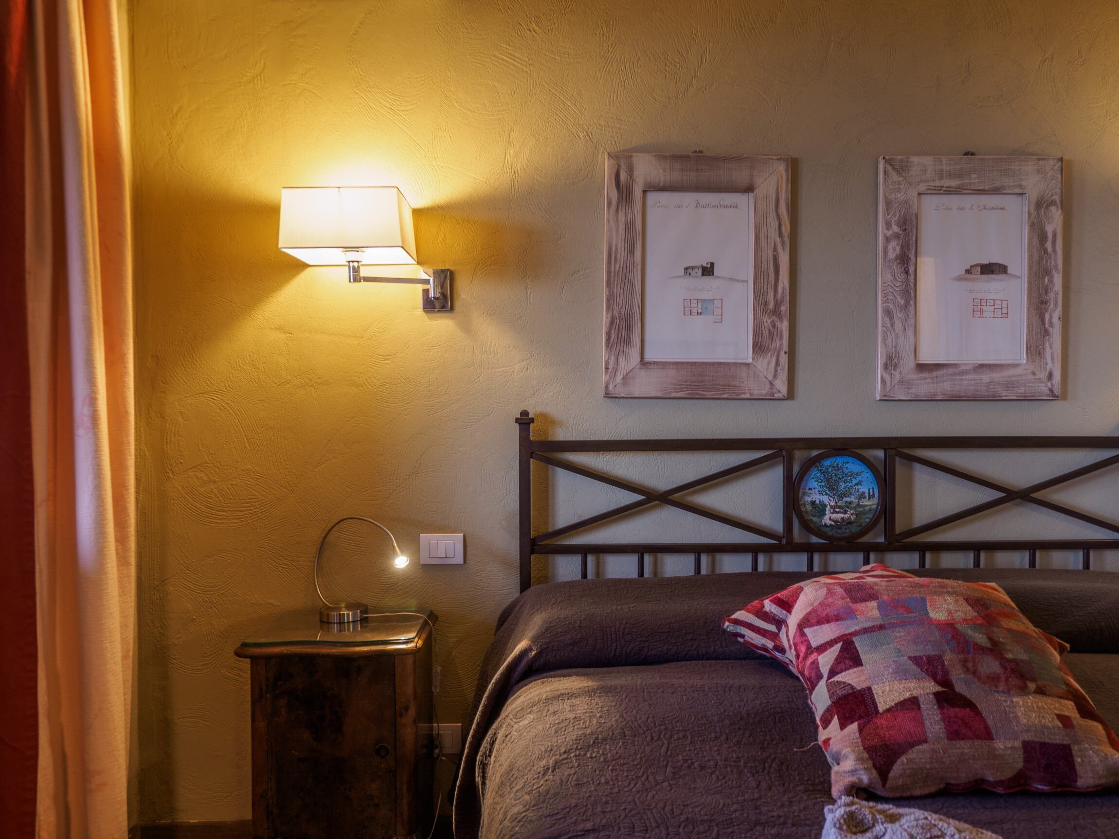 Een slaapkamer met een bed, een nachtkastje met een lamp en twee ingelijste foto’s aan de muur.