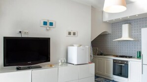 A modern kitchen with white cabinetry, a built-in oven, and a large flat-screen TV.