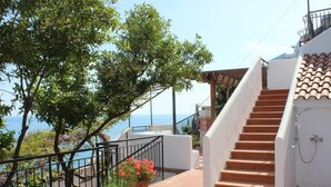 A staircase leading to a balcony overlooking the sea, with a potted plant and a metal railing.