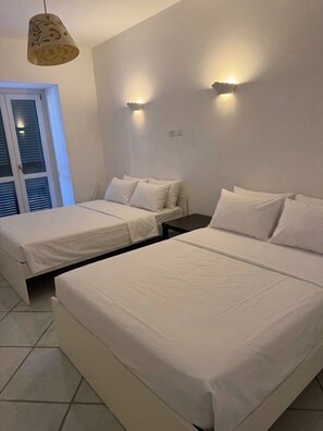 Una habitación de hotel con dos camas, una ventana con persianas y una lámpara fijada a la pared.