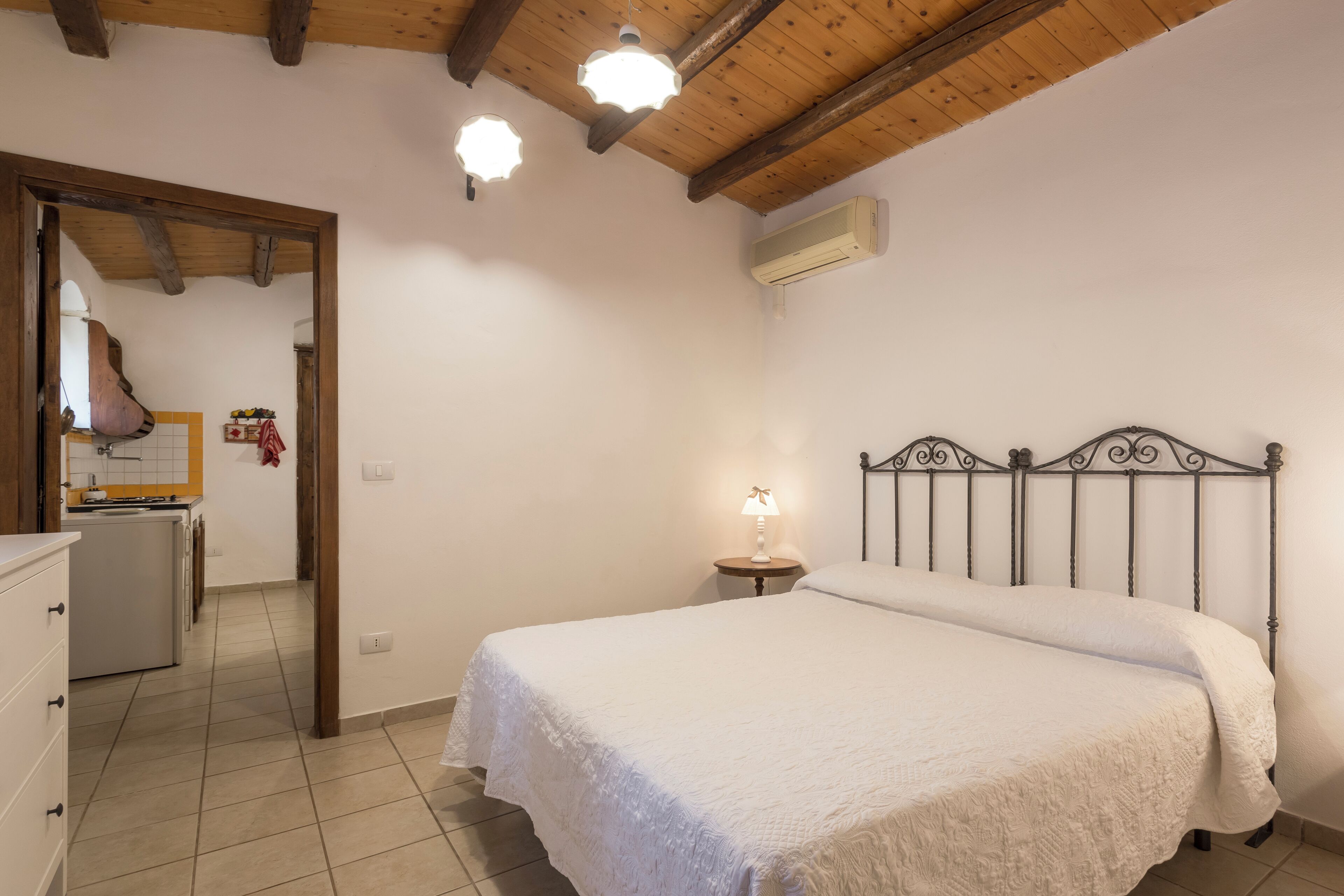 Een slaapkamer met een bed, een bedlamp en een houten plafond.