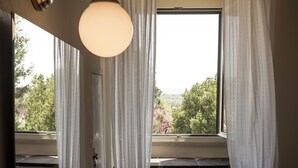 Ein Zimmer mit großem Fenster, weißen Vorhängen und einer runden Leuchte.