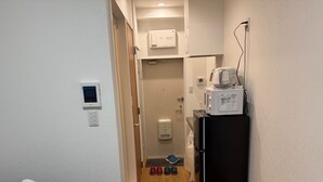 A narrow hallway with a wooden floor, a black refrigerator, a microwave, and a small window.