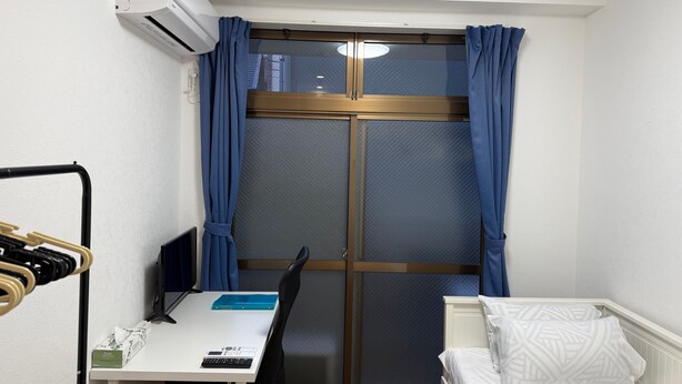 A small room with a bed, a desk with a computer, and a window with curtains.