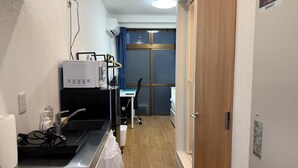 A compact kitchen with a microwave, a small sink, and a window with blue curtains.