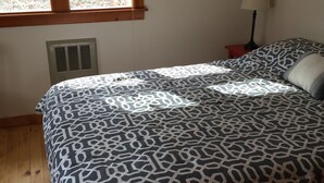 A bedroom with a bed, a window, a wall-mounted picture, and a bedside table with a lamp.