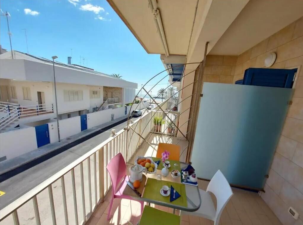 A balcony with a table set for two, a refrigerator, and a view of neighboring buildings.