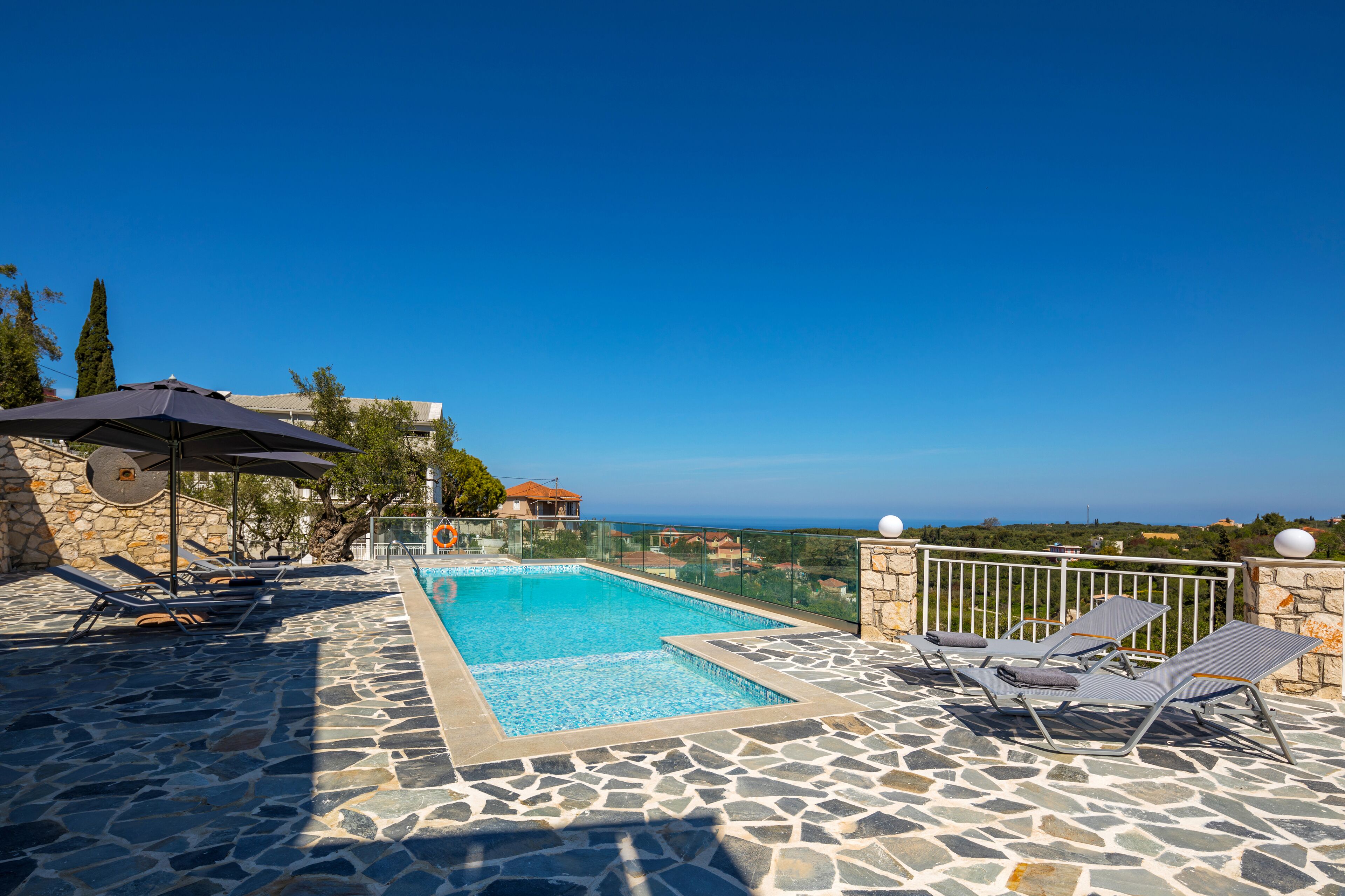 A rooftop swimming pool with stone flooring, lounge chairs, and umbrellas.