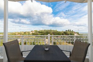 En balkon med et bord og stole, der giver udsigt over et naturskønt landskab med træer og bygninger.