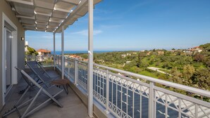 Ein Balkon mit weißer Brüstung, Blick auf das Meer und eine grüne Landschaft.