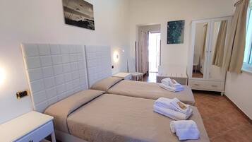 Ein Hotelzimmer mit zwei Betten, einem Nachttisch, einem Sessel, einem Kleiderschrank und einem Bild an der Wand.