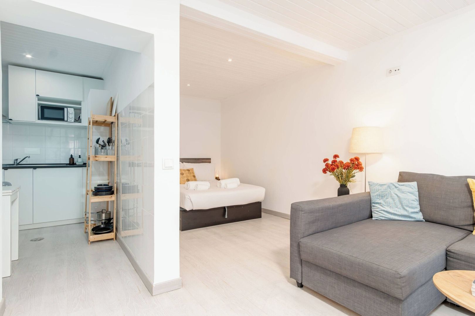 Un apartamento moderno con kitchenette, una cama y un sofá gris.