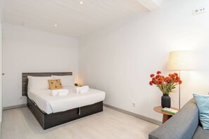 A hotel room with a bed, bedside table, lamp, and a vase of flowers.