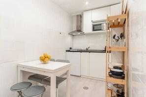 A modern kitchen with white cabinetry, a microwave, a sink, and a wooden shelf with dishes.