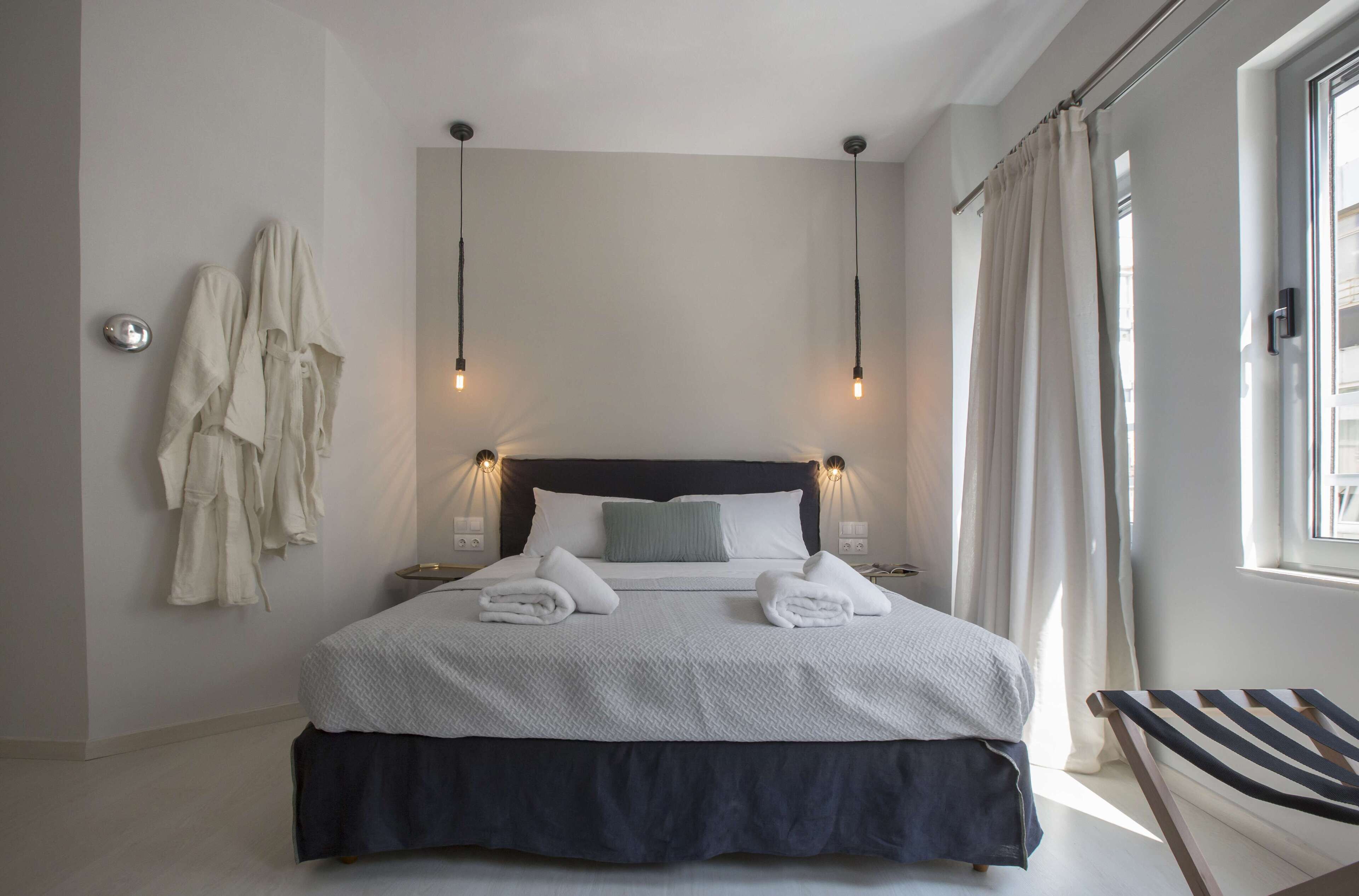 A neatly made bed with towels, a bedside table, and a chair in a modern hotel room with a view of the city.