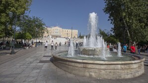 Une place publique avec une fontaine centrale, des bancs en pierre et un grand bâtiment en arrière-plan.