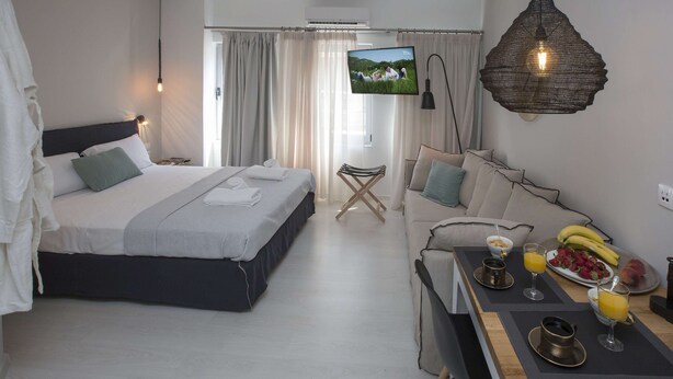 Une chambre d’hôtel moderne avec un grand lit, un canapé, une table à manger où le petit-déjeuner est servi, et un téléviseur fixé au mur.