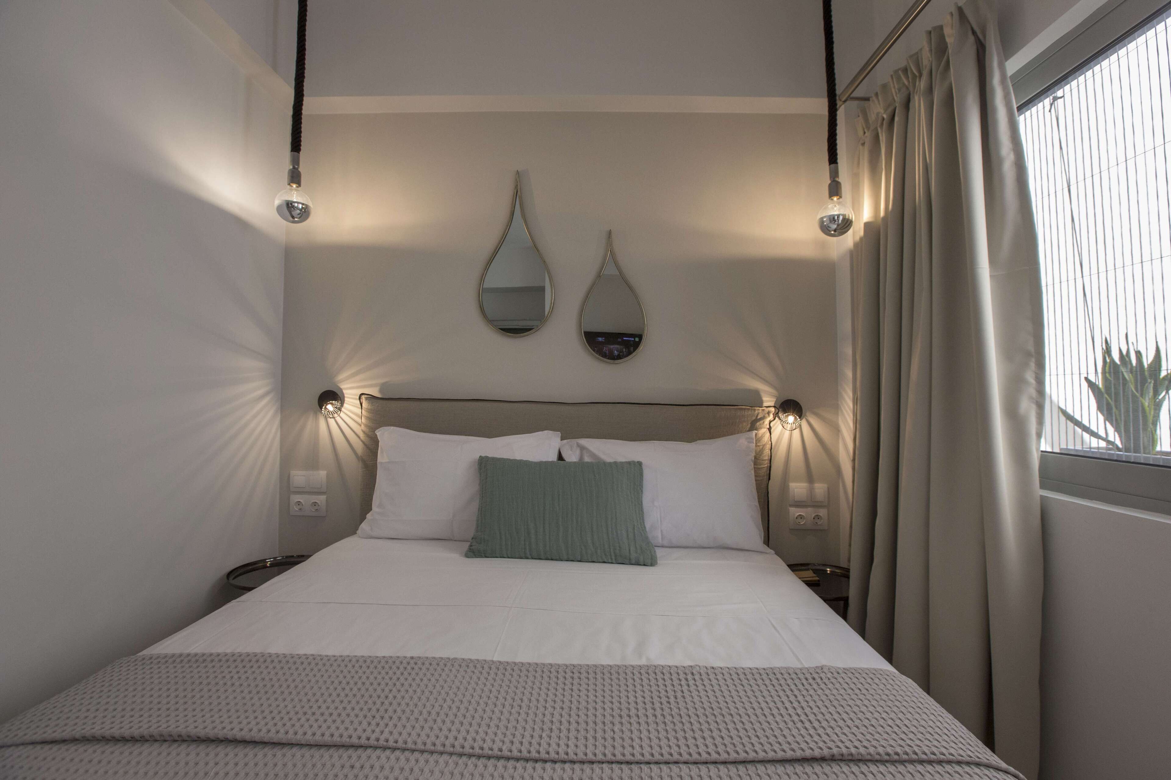 A neatly made bed with a green pillow, two wall-mounted mirrors, and bedside lamps.