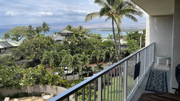 A balcony with a view of a tropical landscape, including palm trees and a body of water.