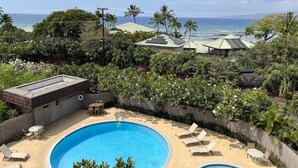 A rooftop pool with two separate sections, surrounded by lush greenery and palm trees, overlooking a beach and ocean.