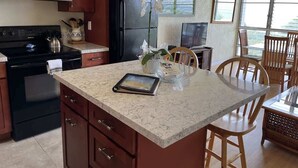 A kitchen with a marble countertop, a refrigerator, an oven, and a dining area with wooden chairs and a table.