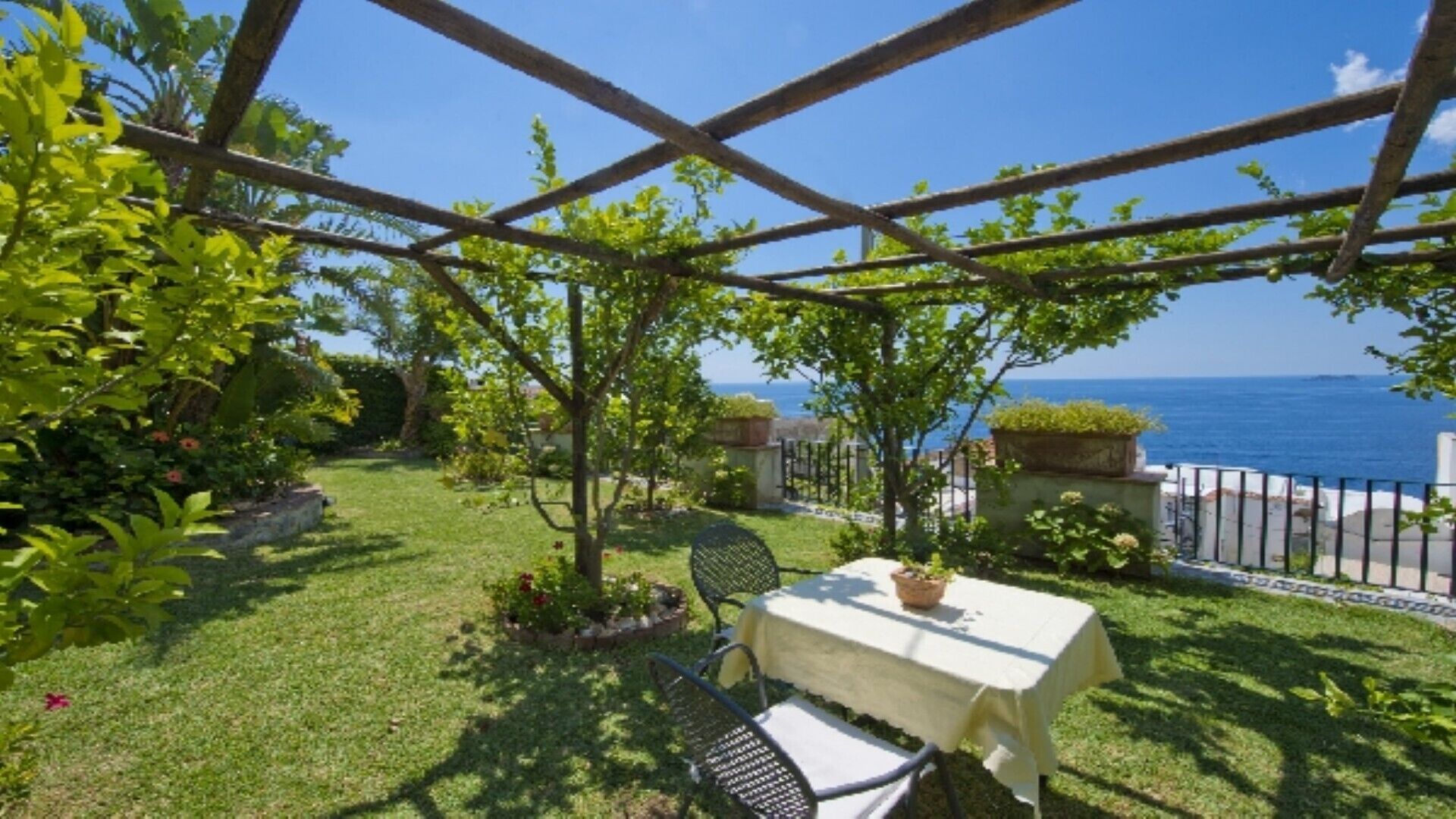 Eine Terrasse mit Tisch und Stühlen mit Blick auf einen Garten und das Meer.